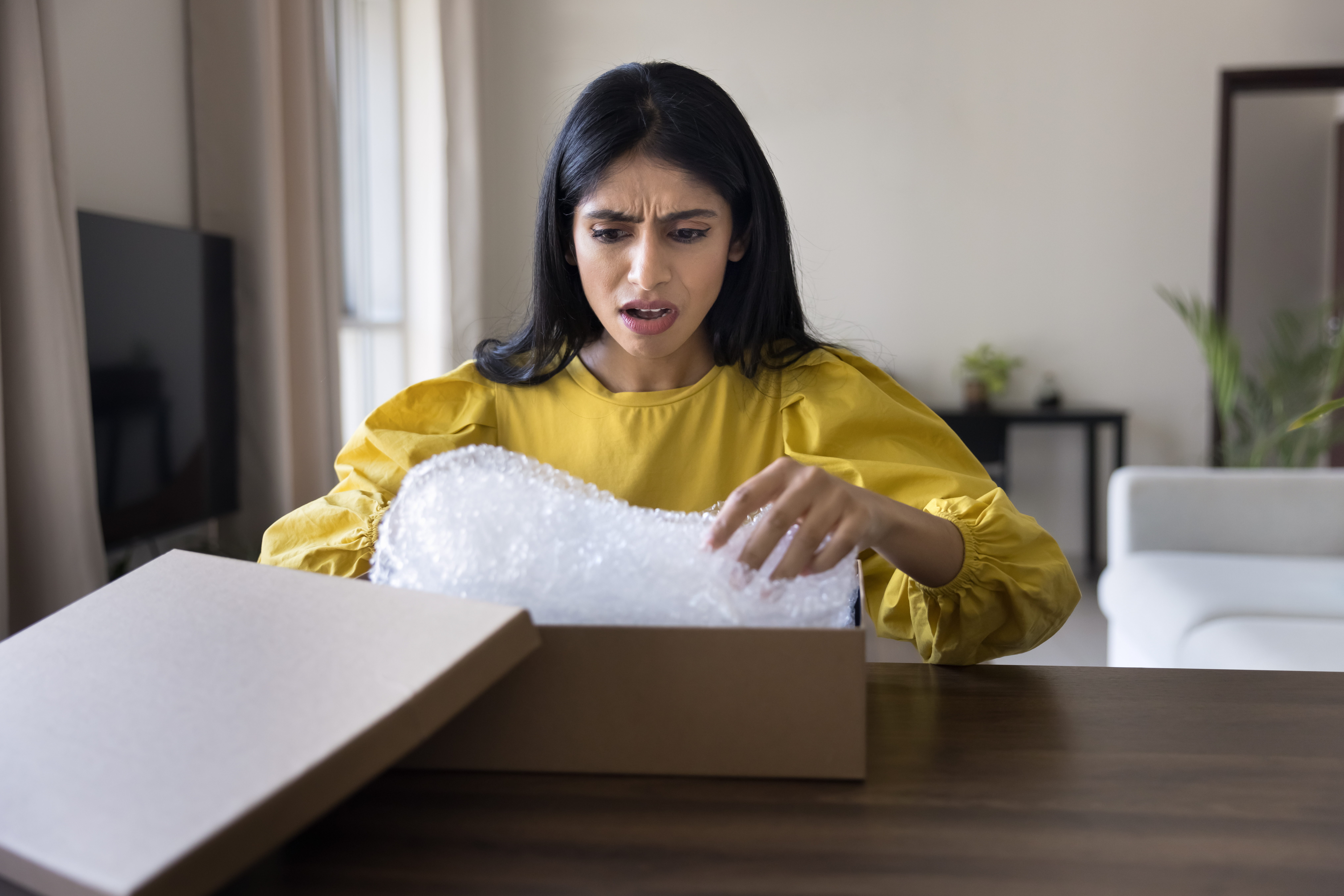Indian woman unboxing package with dissatisfied and shocked expression AdobeStock 1319449391